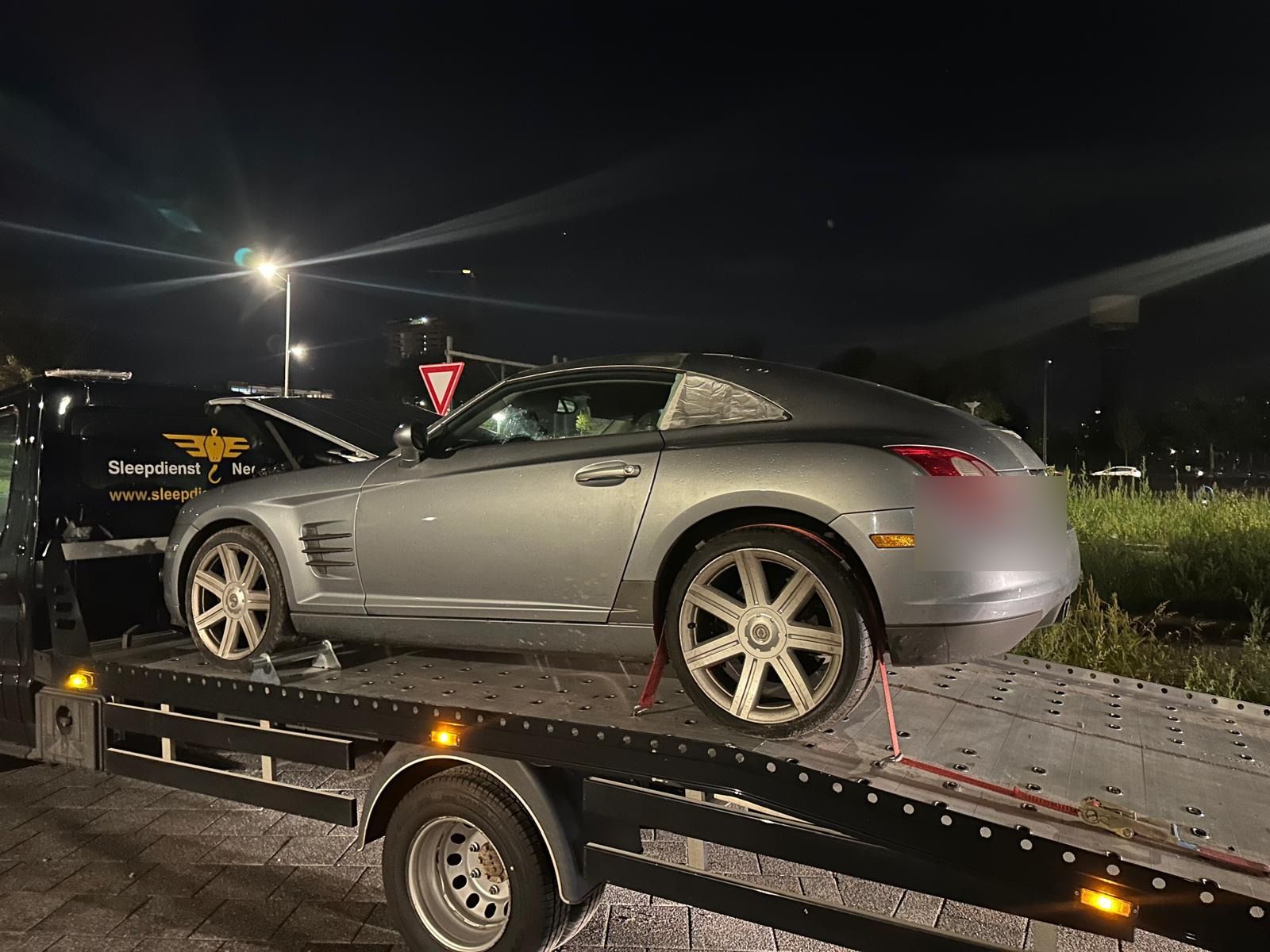 Zilveren sportwagen op de oprijwagen tijdens een nachtelijke sleepopdracht