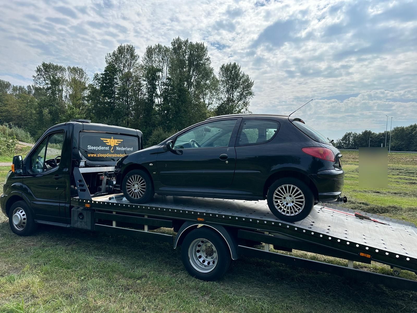 Sleepdienst Nu met een zwarte Peugeot op de oprijwagen langs een landweg