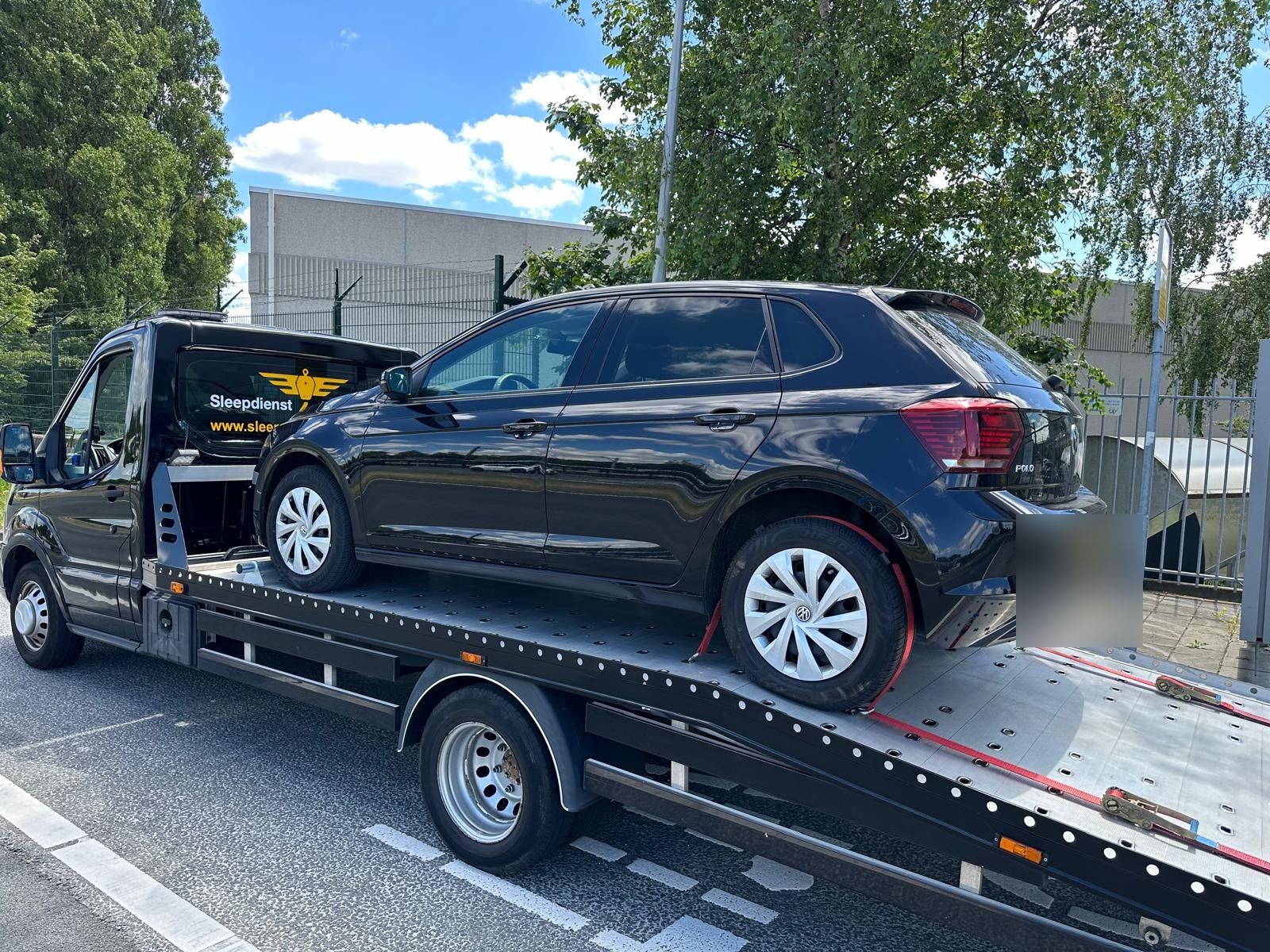 Oprijwagen van Sleepdienst Nu met een zwarte Volkswagen Polo op een bedrijventerrein