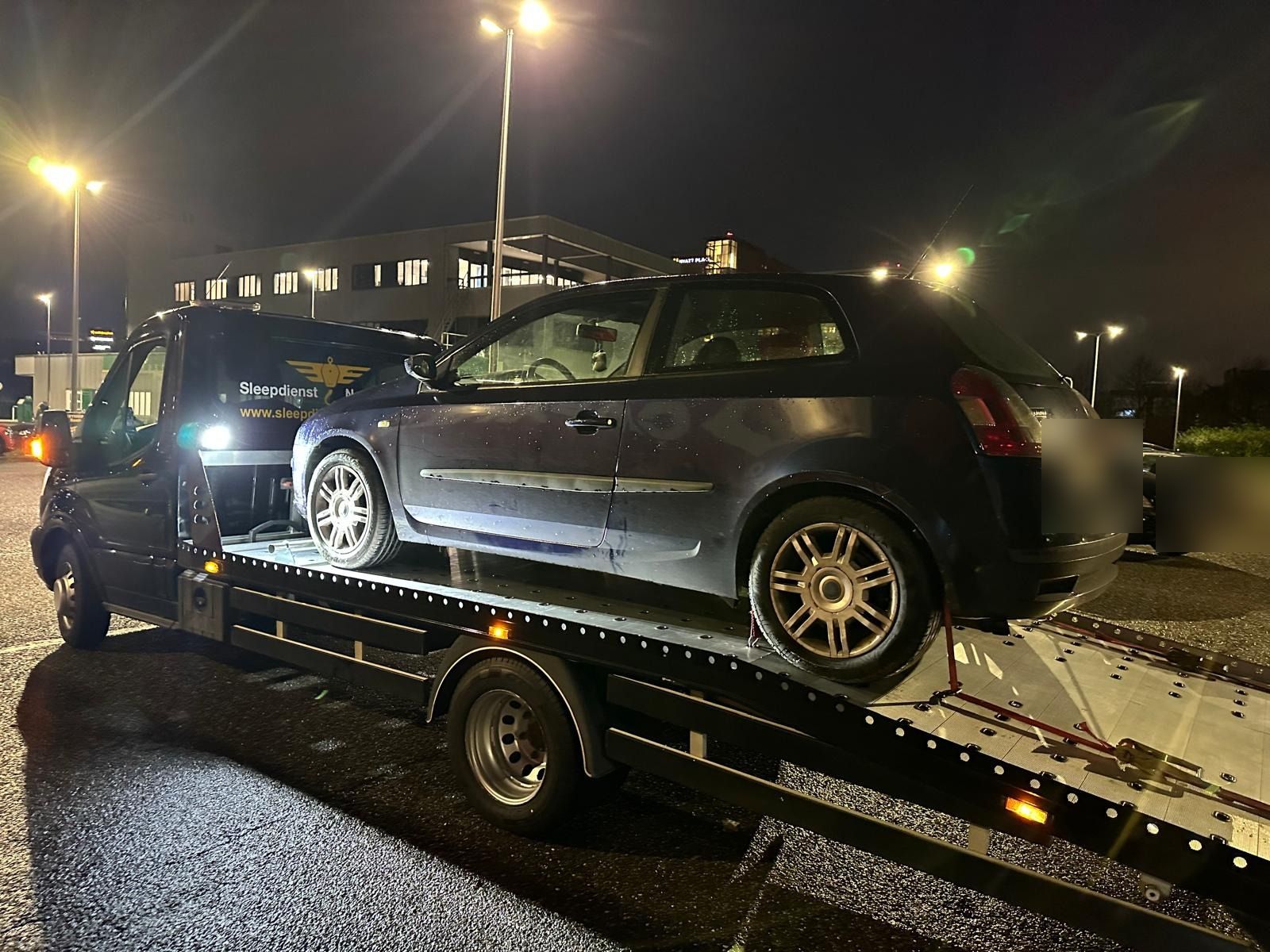 Pechhulp onderweg: zwarte Fiat op de oprijwagen onder straatverlichting