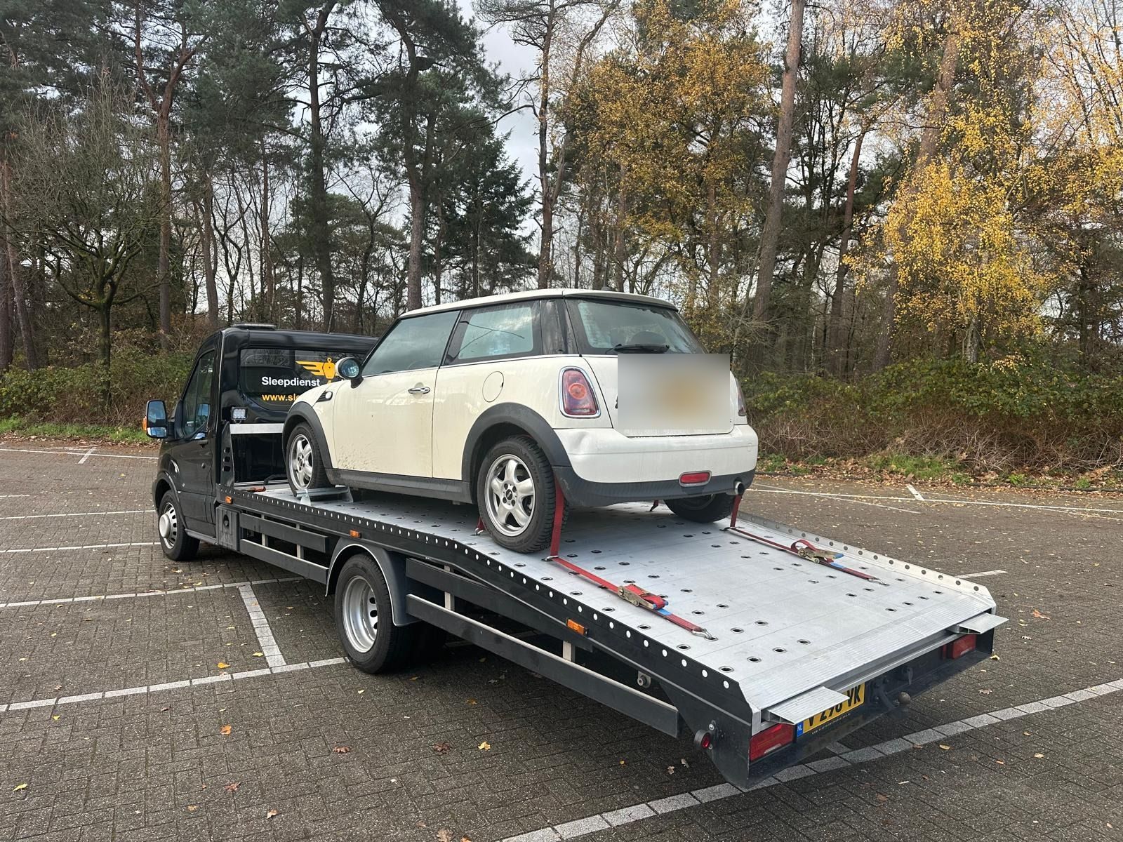 Sleepdienst Nu laadt een witte Mini op een parkeerplaats