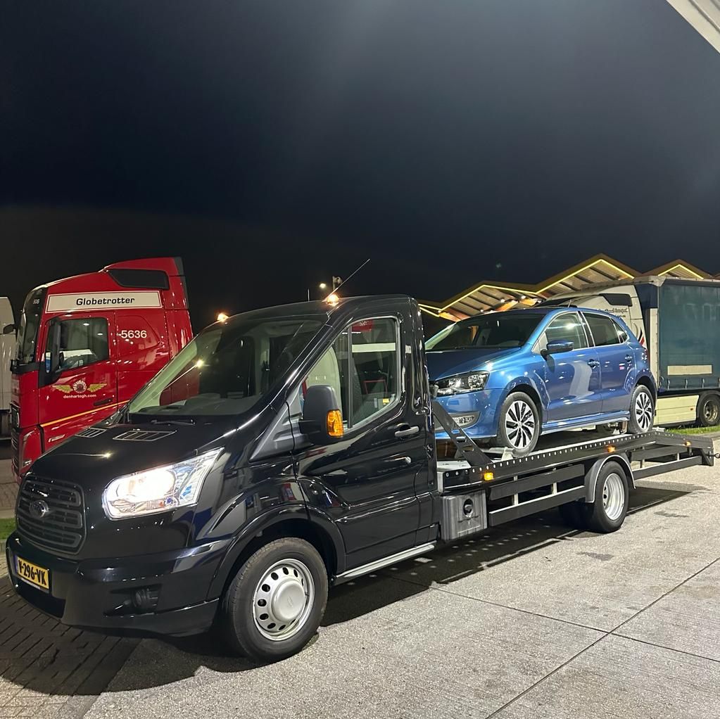 Zwarte takelwagen van Sleepdienst Nu met een opgeladen personenauto, vooraanzicht in het donker